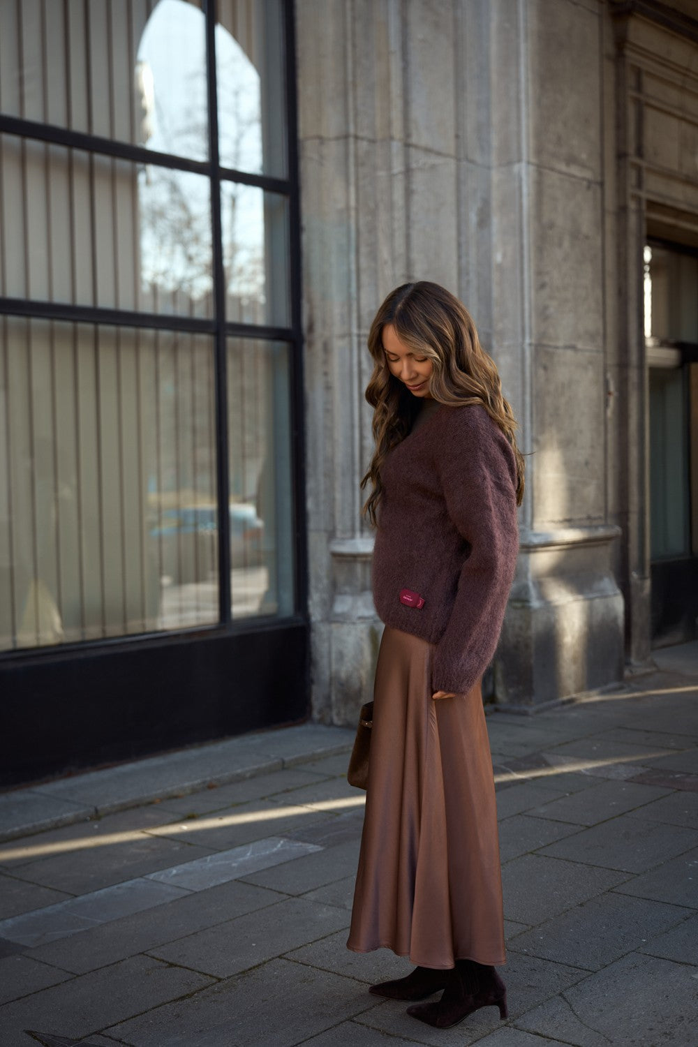 Na zdjęciu widoczna jest brązowa spódnica, która ma elegancki krój, podkreślający sylwetkę. Spódnica jest zestawiona z brązowym swetrem, który jest miękki i przyjemny w dotyku, co nadaje całości przytulny wygląd. Kolory harmonizują ze sobą, tworząc spójną, ciepłą paletę. Stylizacja może być idealna na jesienne dni, łącząc komfort z modnym wyglądem.